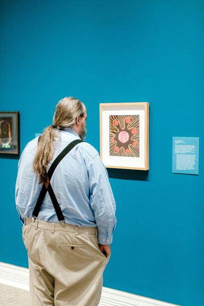 a man from behind looking at a painting on a blue gallery wall