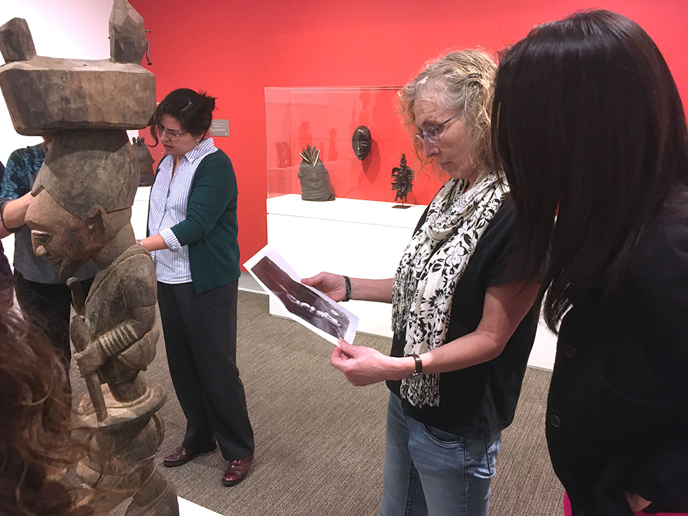 People compare an image on a handout to an African sculpture in a gallery