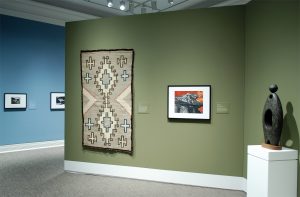 Rug displayed on wall next to framed art and sculpture on stand