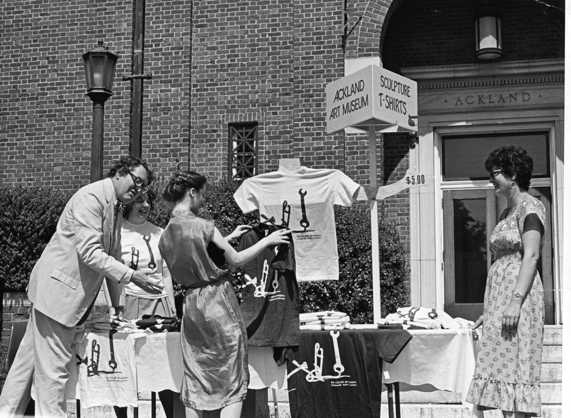 A group of four people looking at t-shirts on a table outdoors