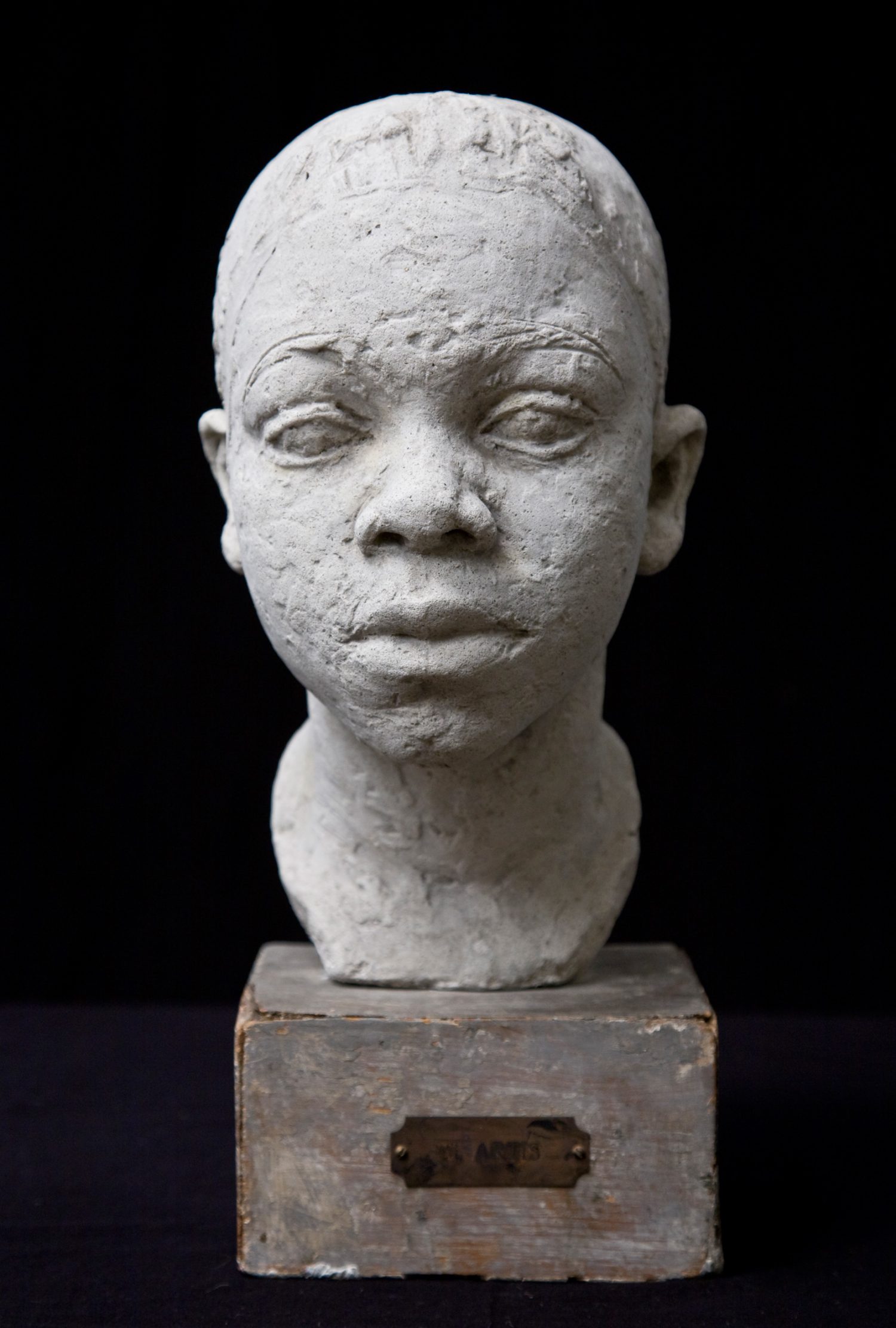 Low-fired clay sculpture of a head of a boy mounted on a wood pedestal