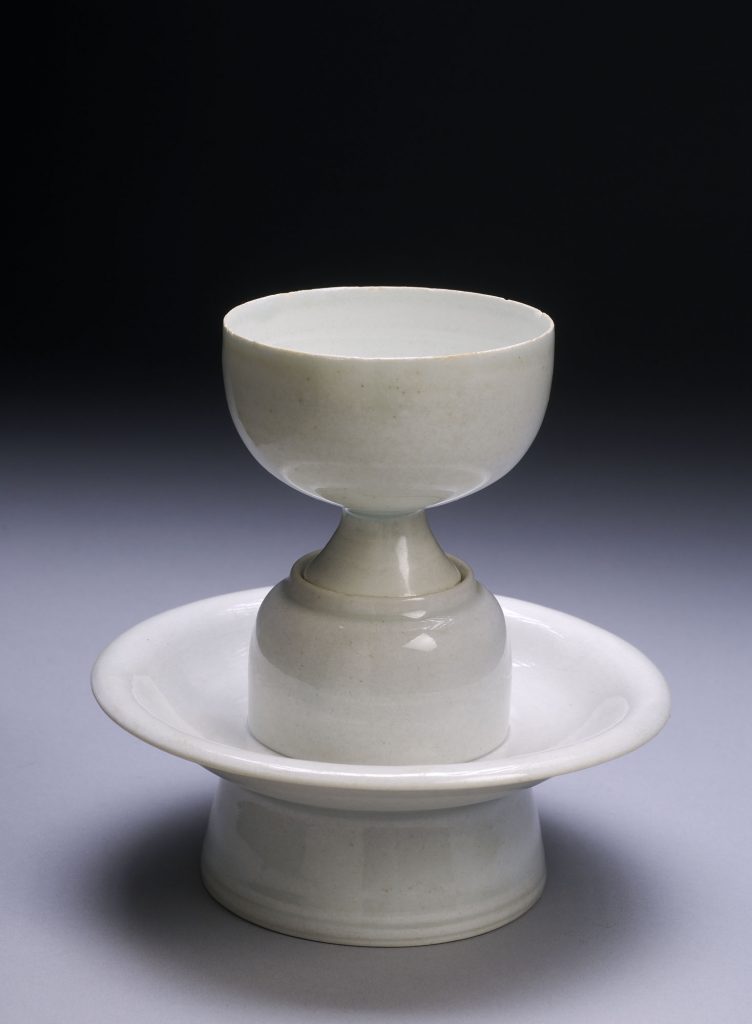 A bluish-white hemispherical cup on a tall foot standing on a saucer-shaped stand with a central pedestal fitted to the foot of the cup. 