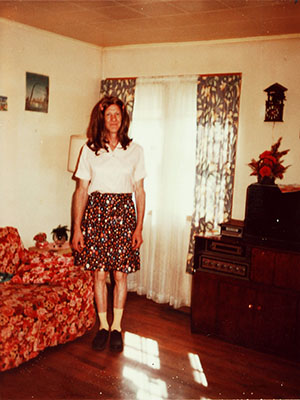 Color photo of a person with light skin wearing a long wig and wearing a skirt and blouse