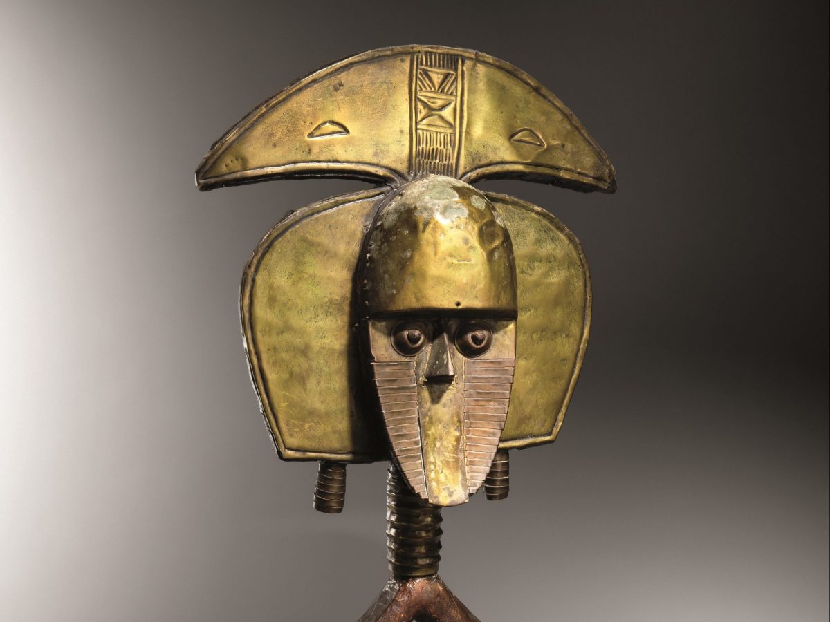 A yellow metal reliquary in the shape of a person's face and upper body