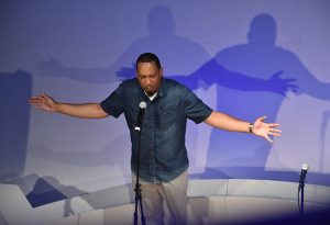 A poet spreads his arms wide as he performs on a stage
