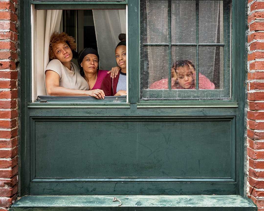A woman and three girls look out of a green-painted window.