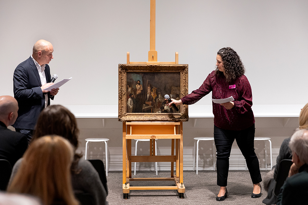 Two people talk about a painting to an audience