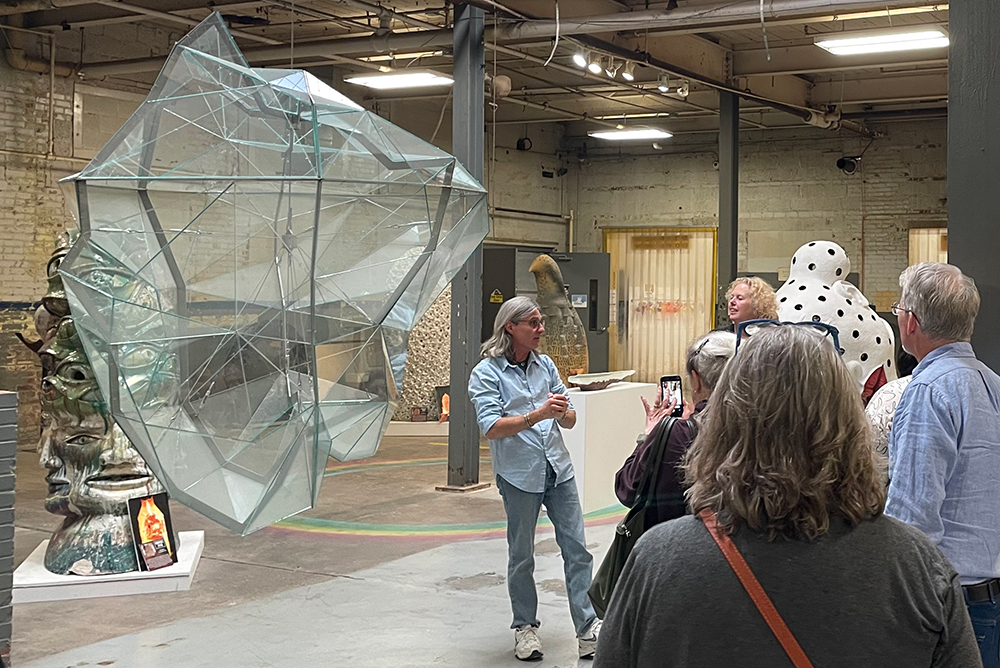 An artist talks about their large steel and plastic sculpture to a group of people